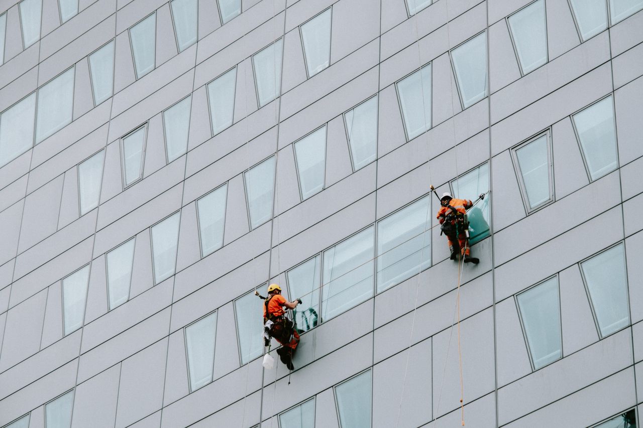 project-02-a High-rise window cleaners in safety gear washing a skyscraper facade.